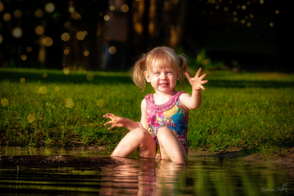 Väike tüdruk suvise järve ääres – lapsepõlve helgus ja looduslik valgus.