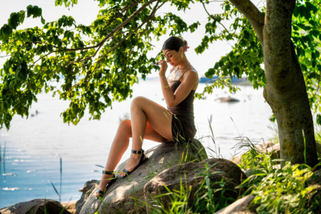 Naise portreefoto kivil istudes mere ääres puude varjus