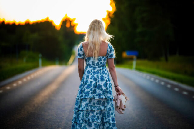 Naise portreefoto teel seistes, seljaga kaamera poole, õhtune valgus