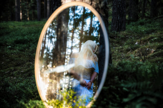 Naise portreefoto ringikujulise peegelraami sees, metsataust